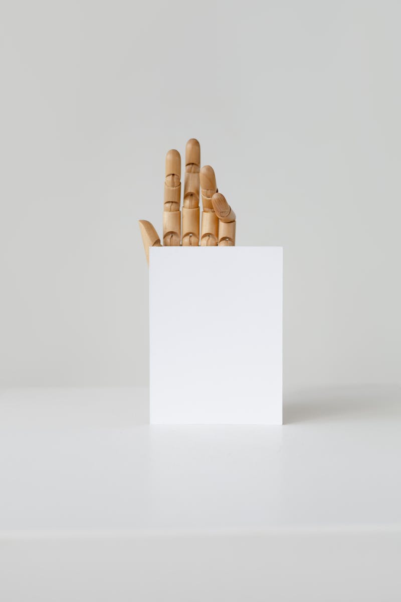 Wooden hand holding a blank card on a neutral background, perfect for mockups and branding.